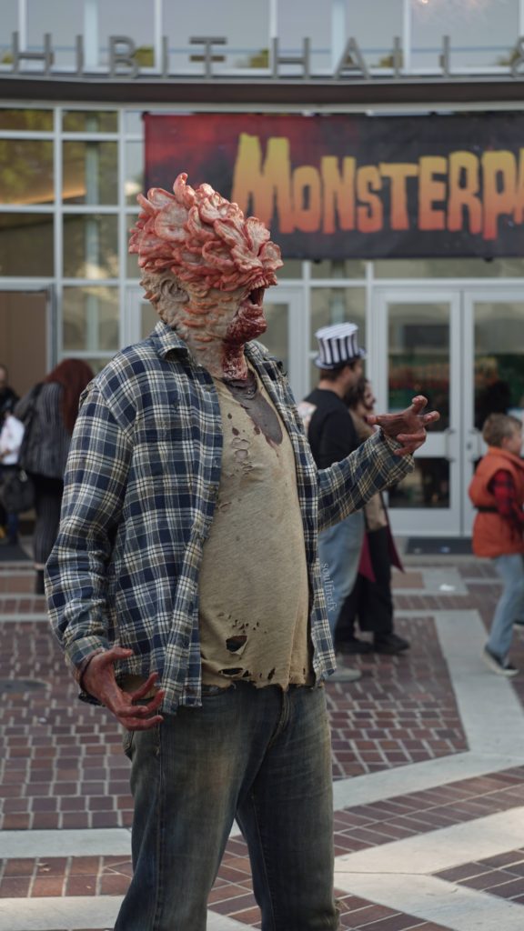 Cordyceps-infested Clicker makeup from The Last of Us, posing in front of the Monsterpalooza convention in 2023.